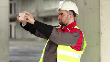 İnşaatçı akıllı telefondan video kaydediyor. İnşaat alanında çalışan biri cep telefonuyla fotoğraf çekiyor.