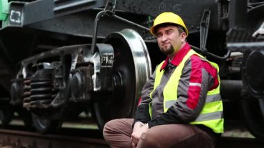 Demiryolu işçisi yük vagonunun yanında oturur ve su içer. Demiryolu işçisi, demiryolu işçisi büyük metal tekerleğin yanında oturur.