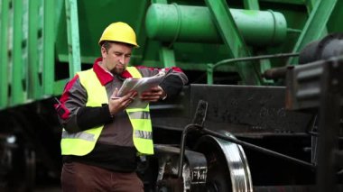 Belgeleri olan bir demiryolu işçisi. Elinde iş planı olan, kasklı bir demiryolu işçisi. Tren istasyonundaki tren trafiği müfettişi not alır. Trenler arasında demiryolu çalışanı