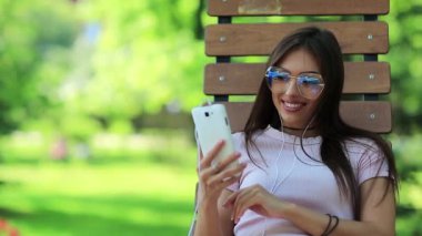 Kadın parkta bankta oturuyor ve akıllı telefon kullanıyor. Büyük gözlüklü bir iş kadını akıllı telefonuna bakıyor, cep telefonu olan bir kız.