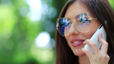 Gözlüklü güzel kız cep telefonuyla konuşuyor, beyaz akıllı telefonlu kadın yakın plan çekiyor. İş kadını cep telefonuyla konuşuyor.