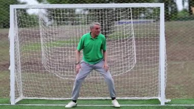 Kaleci futbol sahasında futbol kapısını koruyor. Futbol kapısında aktif yaşlı bir atlet. Son sınıf öğrencisi futbol kalesinde duruyor. Fiziksel aktivite kalori yakmaya yardımcı olur.
