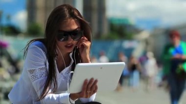 İş kadını çeşmelerin yanında oturur ve tablet bilgisayarla iletişim kurar. Beyaz tabletli gözlüklü çekici bir kadın Skype ya da görüntülü sohbet yoluyla iletişim kuruyor.