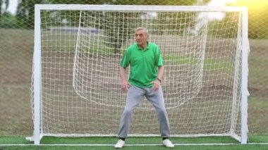 Yaşlı futbolcu futbol kalesinde duruyor. Futbol kapısındaki aktif yaşlı adam. Yeşil tişörtlü kaleci futbol sahasındaki kapıyı koruyor.