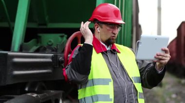 Demiryolu işçisi tablet bilgisayarla konuşuyor. Yük istasyonundaki demiryolu işçisi tablet bilgisayarla görüntülü sohbet yoluyla konuşuyor