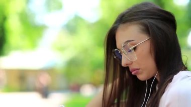 Akıllı telefon ve kulaklıklı çekici bir kadın müzik dinliyor. Akıllı telefonlu kız parkta müzik dinliyor.
