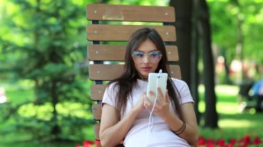 Kız şehir parkında bankta oturuyor ve akıllı telefon kullanıyor. Büyük gözlüklü bir iş kadını akıllı telefonuna bakıyor, cep telefonu olan bir kadın.