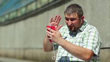 Komik adam akıllı telefonla konuşuyor. Akıllı telefonlu neşeli adam Skype üzerinden iletişim kuruyor ve el kol hareketi yapıyor. Elinde kırmızı cep telefonu olan, kareli tişörtlü, şişman, şen şakrak adam.