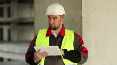İnşaatçı proje sitesinde tablet bilgisayarla çalışıyor. İnşaat alanında tablet bilgisayarı olan bir işçi. Beyaz başlıklı işçi elinde kişisel bilgisayarla, ekranda görünüyor.