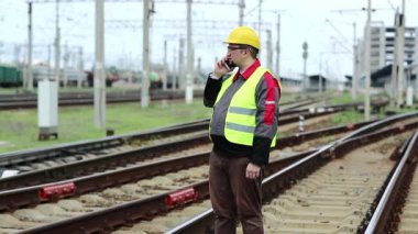 Demiryolu çalışanı cep telefonuyla konuşuyor. Demiryolu işçisi demiryolu hattında duruyor ve cep telefonuyla konuşuyor, demiryolu işçisi akıllı telefonuyla iletişim kuruyor.