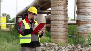 Sarı başlık konusunda uzman güç mühendisi. Belgelerle çalışıyor. İşçi, ana boru hattı yakınlarındaki ısı elektrik santrali hakkında notlar alıyor
