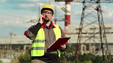Elektrik santralindeki işçiler akıllı telefondan konuşuyor. Sarı başlıklı, cep telefonlu ve elektrik santralinde çalışan elektrik mühendisliği uzmanı.