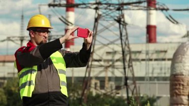Powerman akıllı telefondan video kaydediyor. Elektrik santralinde çalışan, sarı şapkalı, akıllı telefonlu bir işçi.