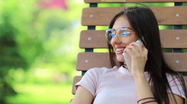 Güzel bir kadın bankta oturur ve cep telefonuyla konuşur. Akıllı telefonlu bir iş kadını halka açık bir bahçede oturur. Çekici kız cep telefonuyla konuşuyor, beyaz akıllı telefonlu bir kadın.