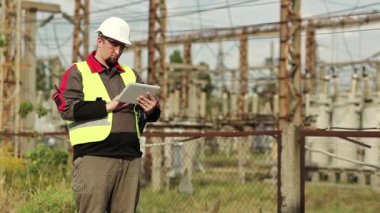 Güç istasyonunda tablet bilgisayarı olan bir Powerman. Elektrik santralindeki beyaz başlıklı işçi, mühendislik denetimi. Tablet bilgisayarlı fabrika işçisi