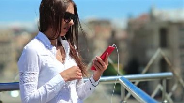 Kız akıllı telefon kullanıyor. Uzun saçlı, güneş gözlüklü, kırmızı cep telefonlu güzel bir kadın.