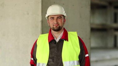 İşçi kameraya bakar. Beyaz şapkalı bir mimar proje sitesinde duruyor ve kameraya bakıyor.