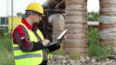 Elektrik mühendisliği uzmanı sarı başlık tabletle çalışıyor. Ana boru hattının yakınındaki ısı elektrik santralinde tablet bilgisayarı olan bir işçi.