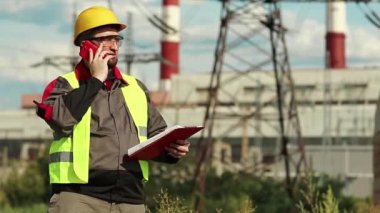 Elektrik santralindeki işçiler akıllı telefondan konuşuyor. Sarı başlıklı, cep telefonlu ve elektrik santralinde çalışan elektrik mühendisliği uzmanı.