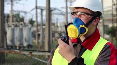 Elektrikçi, taşınabilir radyo vericisiyle elektrik santralinde. Gaz maskesi, gözlükler ve ısı santralinin başlığı konusunda uzman olan elektrik mühendisi radyo istasyonu aracılığıyla iletişim kuruyor.