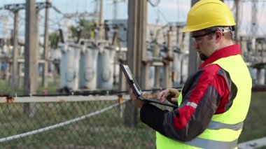 Elektrik santralinde bilgisayarı olan bir elektrikçi. Elektrik santralinde baret takan bir işçi, mühendislik denetimi. Tablet bilgisayarlı fabrika işçisi