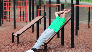 Kıdemli adam karın kaslarını şişiriyor ve kalorileri yakıyor. Aktif, gri saçlı, yeşil tişörtlü sporcu spor sahasında fiziksel egzersiz yapıyor açık hava spor salonunda antrenman yapıyor.