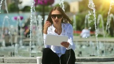 İş kadını çeşmelerin yanında oturur ve tablet bilgisayarla iletişim kurar. Beyaz tablet bilgisayarlı gözlüklü çekici bir kadın video kaset aracılığıyla iletişim kuruyor.