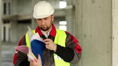 İnşaat belgeleriyle birlikte inşaat müfettişi. İnşaat alanındaki çalışma kağıtlarıyla birlikte beyaz şapkalı usta müteahhit.