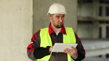 İnşaat alanında tablet bilgisayarı olan bir işçi. İnşaatçı proje sitesinde tablet bilgisayarla çalışıyor. Beyaz başlıklı işçi elinde kişisel bilgisayarla, ekranda görünüyor.