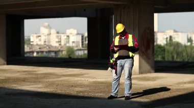 İnşaat alanında çalışan bir işçi. İnşaat müfettişi proje sahasında inşaat belgelerine sahip, inşaatçı notlar yazıyor