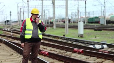 Demiryolu işçisi, demiryolu terminali yakınında taşınabilir radyo vericisi var. Demiryolu çalışanı, nakliye istasyonunun yanındaki demiryolu hattında portatif radyo vericisi aracılığıyla konuşuyor. İşçi radyo istasyonu aracılığıyla iletişim kuruyor.