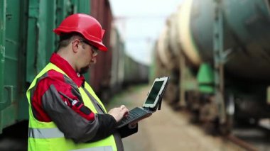 Trenler arasında tablet bilgisayarlı demiryolu işçisi. Tren istasyonundaki tren trafiği müfettişi tablet bilgisayarına not alır.