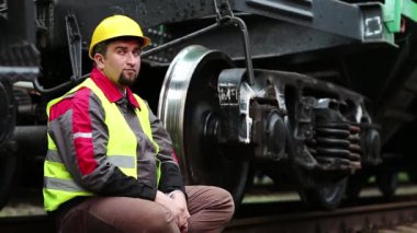Demiryolu işçisi yük vagonunun yanında oturur ve su içer. Demiryolu işçisi, demiryolu işçisi büyük metal tekerleğin yanında oturur.