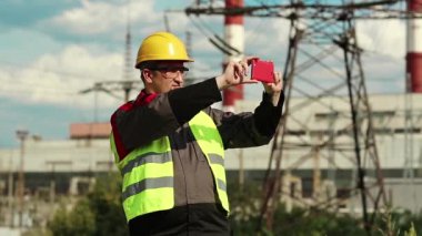 Powerman kırmızı akıllı telefondan video kaydediyor. Elektrik santralinde çalışan sarı şapkalı, akıllı telefonlu bir işçi.