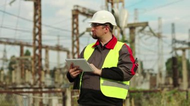 Elektrik santrali üzerine tablet bilgisayarı olan güçlü bir adam. Elektrik istasyonunda beyaz şapkalı bir işçi, mühendislik denetimi. Tablet bilgisayarlı fabrika işçisi