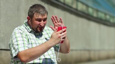 Komik adam akıllı telefonla iletişim kuruyor. Akıllı telefonlu neşeli adam Skype üzerinden iletişim kuruyor ve el kol hareketi yapıyor. Elinde kırmızı cep telefonu olan, kareli tişörtlü, şişman, şen şakrak adam.