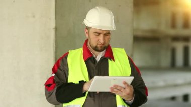 İnşaat alanında tablet bilgisayarı olan bir işçi. İnşaatçı proje sitesinde tablet bilgisayarla çalışıyor. Beyaz başlıklı işçi elinde kişisel bilgisayarla, ekranda görünüyor.