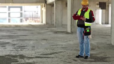 İnşaat alanında denetleyici personel. Proje alanında sarı şapkalı bir müfettiş. Mühendislik denetimi, inşaatçı notlar yazar