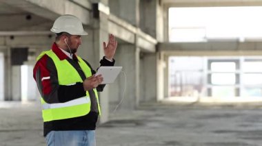 İnşaat alanında tablet bilgisayarı olan bir işçi. İnşaatçı proje sitesindeki tablet bilgisayarla konuşuyor. Beyaz başlıklı işçi elinde kişisel bilgisayarla, ekranda görünüyor.
