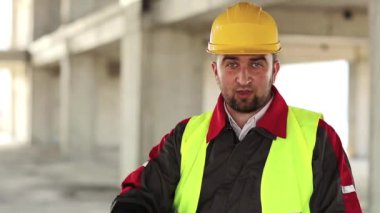 Kızgın ama komik inşaatçı kamerada konuşuyor. İşçi inşaat alanında durup kameraya bakar ve konuşur.