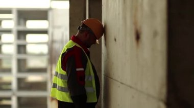 Mimar kafasını duvara vuruyor. Başlıklı stresli işçi inşaat sahasında duruyor ve kafasını beton duvara vuruyor, kendini kınıyor ve kendini kınıyor.