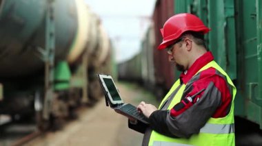 Yük trenlerinin yanında tabletli bir demiryolu işçisi. Tren istasyonundaki tren trafiği müfettişi tablet bilgisayarına not alır.