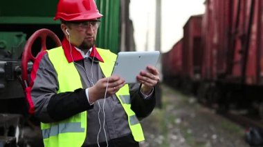 Demiryolu işçisi, yük trenleri arasında tablet bilgisayarla konuşur. Yük istasyonundaki demiryolu işçisi tablet bilgisayarla görüntülü sohbet yoluyla konuşuyor