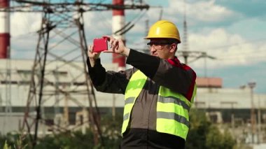 İşçi akıllı telefondan video kaydediyor. Elektrik santralinde akıllı telefonlu sarı şapkalı güçlü adam.