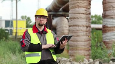 Elektrik mühendisliği uzmanı sarı başlık tabletle çalışıyor. Ana boru hattının yakınındaki ısı elektrik santralinde tablet bilgisayarı olan bir işçi.