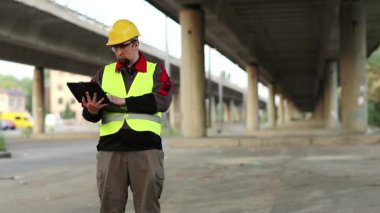 Üstgeçidin altında kişisel bilgisayarı olan bir işçi. Tamirat müdürü inşaat sahasında çalışıyor. Ana yolun altında. Bilgisayarına veri giriyor.