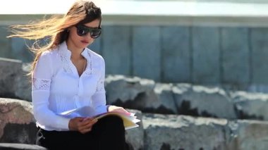 Ticari evrakları olan kızgın ve stresli bir kadın. Sinirli genç kadın şehir merkezindeki büyük merdivenlerde oturuyor ve elinde iş belgeleriyle geziyor, rüzgar ona esiyor.