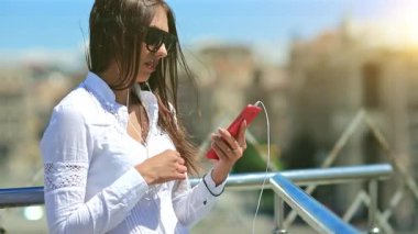 Genç bayan kırmızı akıllı telefon kullanıyor. Uzun saçlı, güneş gözlüklü, kırmızı akıllı telefonlu güzel bir kız.