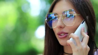 Akıllı telefonlu bir iş kadını, yakın plan. Kız cep telefonuyla konuşuyor. Gözlüklü güzel bir kadın cep telefonuyla konuşuyor, beyaz akıllı telefonlu bir kadın.