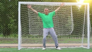 Son sınıf öğrencisi futbol kalesinde duruyor. Futbol kapısında aktif yaşlı bir atlet. Yeşil tişörtlü kaleci futbol sahasındaki kapıyı koruyor. Fiziksel aktivite kalori yakmaya yardımcı olur.